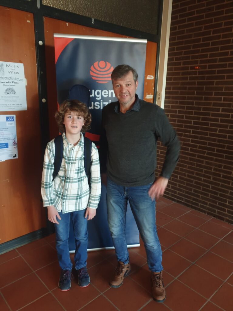 Anton H. Gitarren-Schüler der Musikschule mit Peter Neuhof beim Jugend Musiziert Wettbewerb 2024 stehend vor Banner